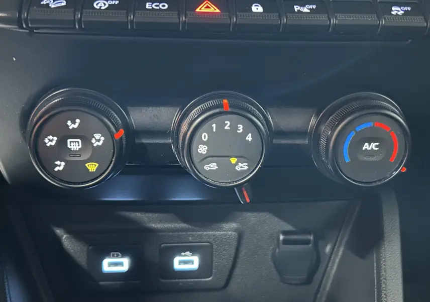 Vue rapprochée du tableau de bord du Dacia Duster 2024 montrant les commandes de climatisation et deux ports USB éclairés.