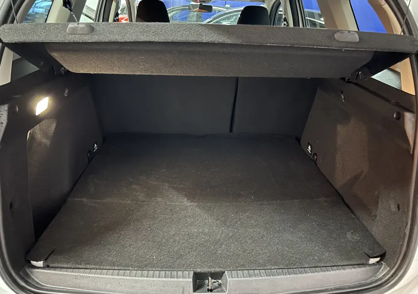 Vue intérieure du coffre ouvert d'un Dacia Duster blanc, avec cache-bagages en position et sièges arrière visibles.