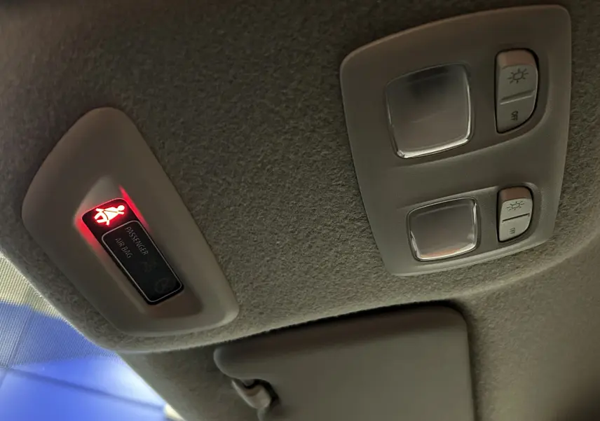 Détail du plafonnier intérieur avec témoin airbag passager allumé et commandes d’éclairage sur Dacia Duster blanc.