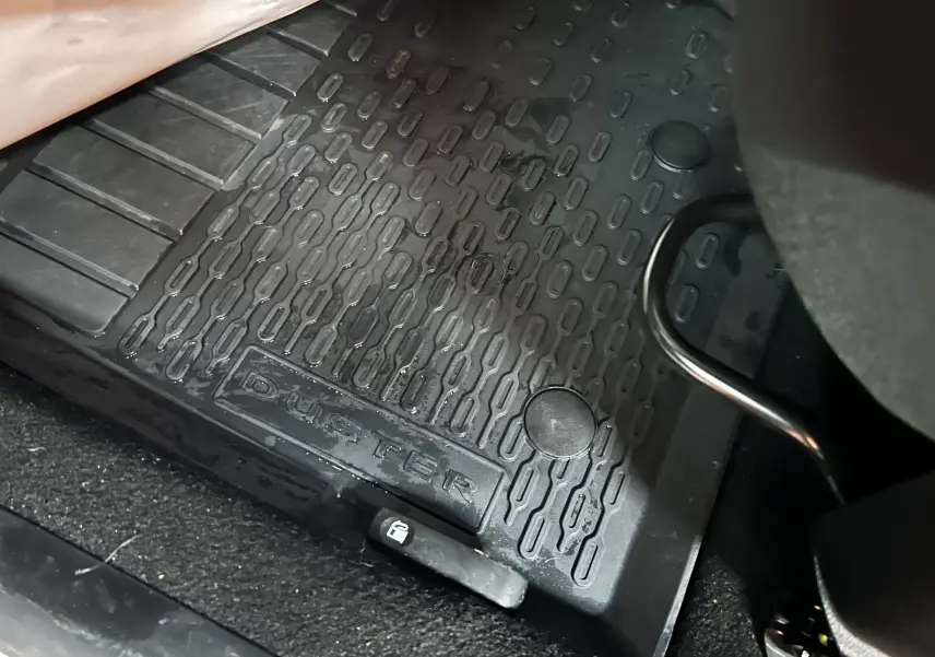 Tapis de sol noir avec inscription DUSTER en gros plan à l'avant droit d'un Dacia Duster blanc 2024.