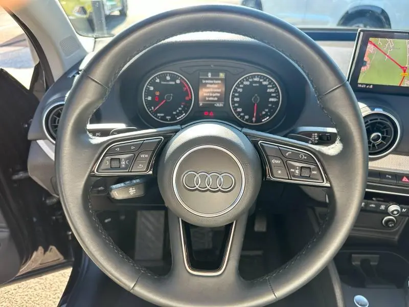 Vue intérieure centrée sur le volant cuir multifonction d’un Audi Q2 blanc avec tableau de bord et écran GPS visible.