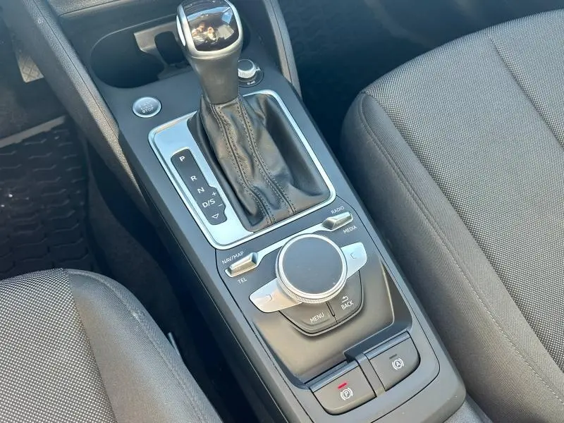Gros plan sur la console centrale noire avec levier de vitesse automatique et commandes multimédia d'un Audi Q2 blanc.