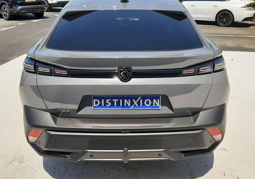 Vue arrière d'une Peugeot 408 HYBRID gris selenium 2024 avec feux LED étirés et logo lion central noir.