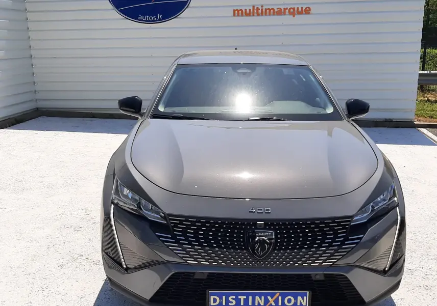 Vue avant d'une Peugeot 408 Hybrid gris sélénium avec calandre noire et logo lion central, stationnée devant un mur blanc.