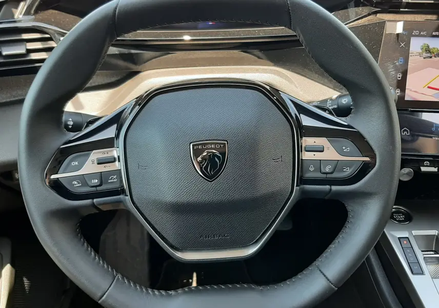 Vue rapprochée du volant cuir noir du Peugeot 408 Hybrid 2024 avec commandes intégrées et tableau de bord numérique.