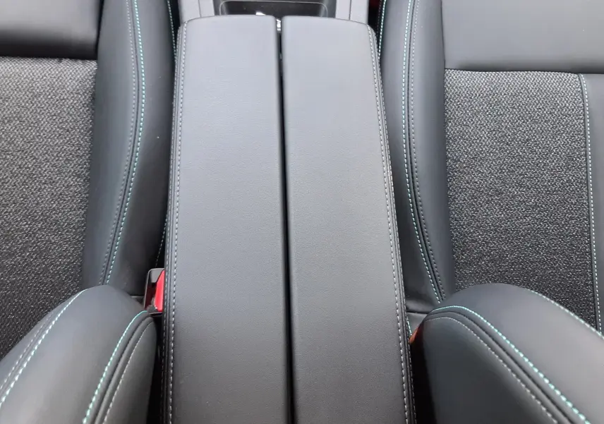 Vue plongeante sur l'accoudoir central en cuir noir avec surpiqûres bleues et sièges tissu et cuir gris du Peugeot 408 2024.