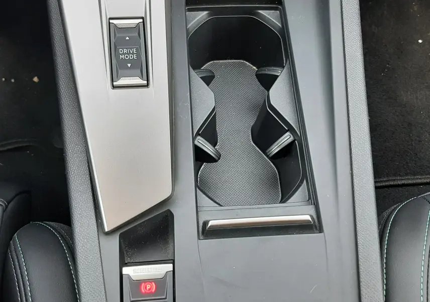 Vue plongeante sur la console centrale noire de la Peugeot 408 Hybrid 2024 avec porte-gobelets et bouton Drive Mode.