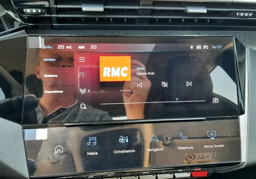 Vue rapprochée de l’écran tactile central du tableau de bord du Peugeot 408 gris, affichant la radio RMC et les commandes multimédia.