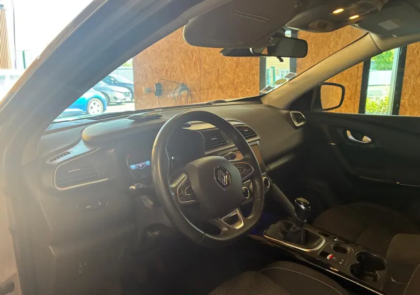 Vue intérieure côté conducteur du Renault Kadjar gris, montrant le volant, la console centrale avec boîte manuelle et tableau de bord.