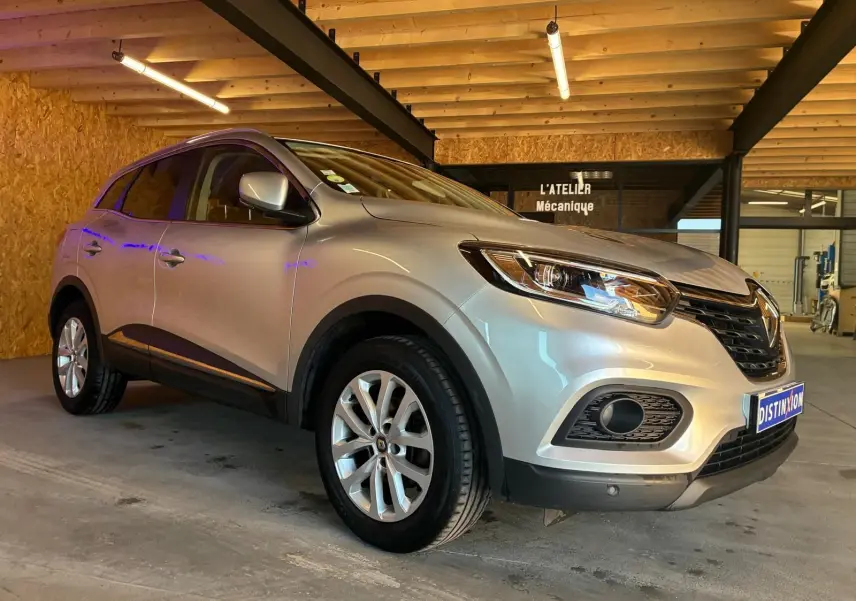Renault Kadjar gris 3/4 avant droit, SUV compact avec jantes alliage et calandre noire, en intérieur d'atelier mécanique.