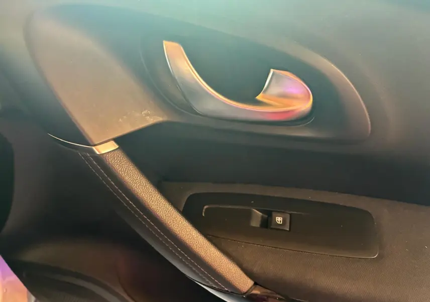 Poignée de porte intérieure côté gauche en métal brossé avec bouton de commande de vitre sur Renault Kadjar gris, vue rapprochée.