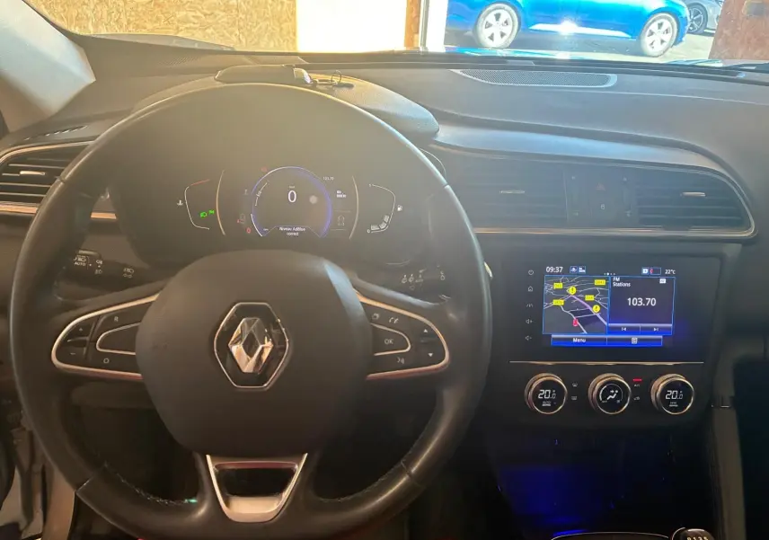 Vue intérieure centrée sur le volant Renault et le tableau de bord avec écran tactile et climatisation digitale du Kadjar gris.