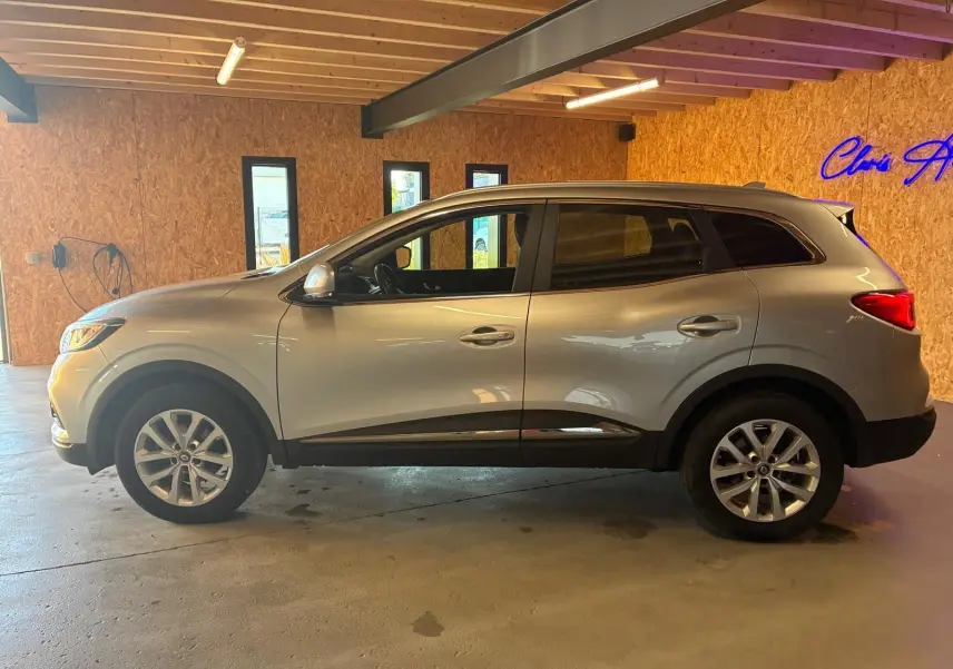 Profil côté gauche d'un Renault Kadjar gris 2020, version 1.5 BlueDCI 115 Business, dans un garage en bois.