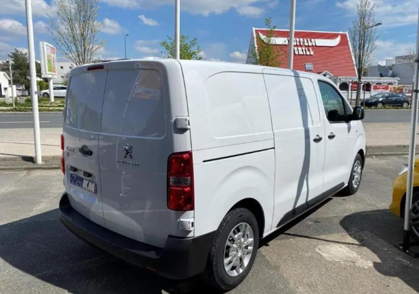 Vue 3/4 arrière droite d'un Peugeot Expert Fourgon blanc stationné en extérieur sous un ciel bleu.