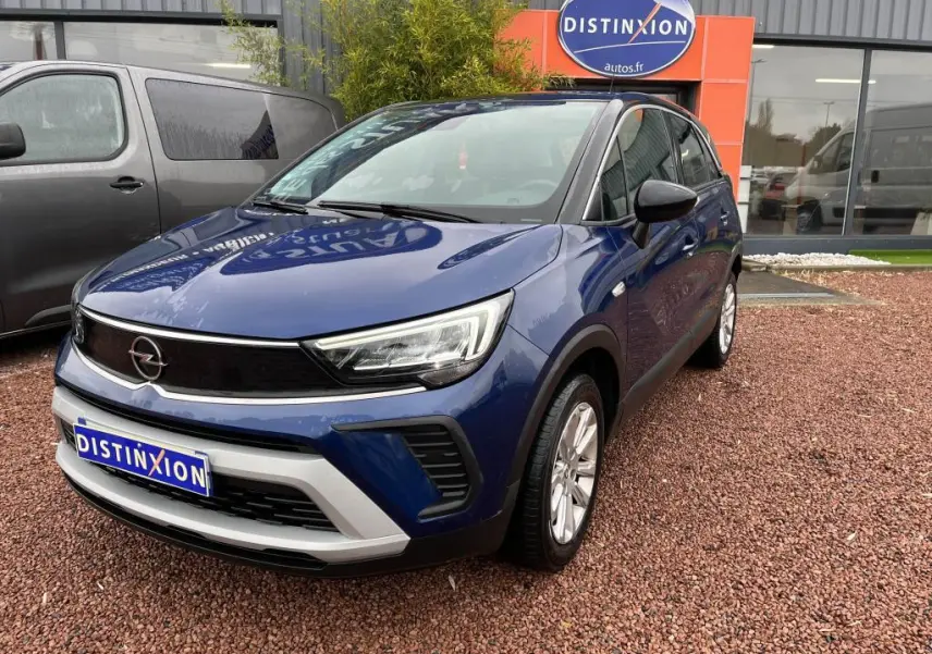 Opel Crossland bleu clair en 3/4 avant droit avec toit noir, stationné devant un bâtiment commercial.