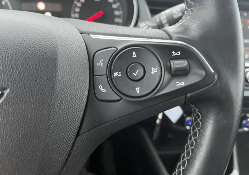 Gros plan sur les commandes au volant noir de l'Opel Crossland bleu clair 2021, avec boutons de volume et appels.