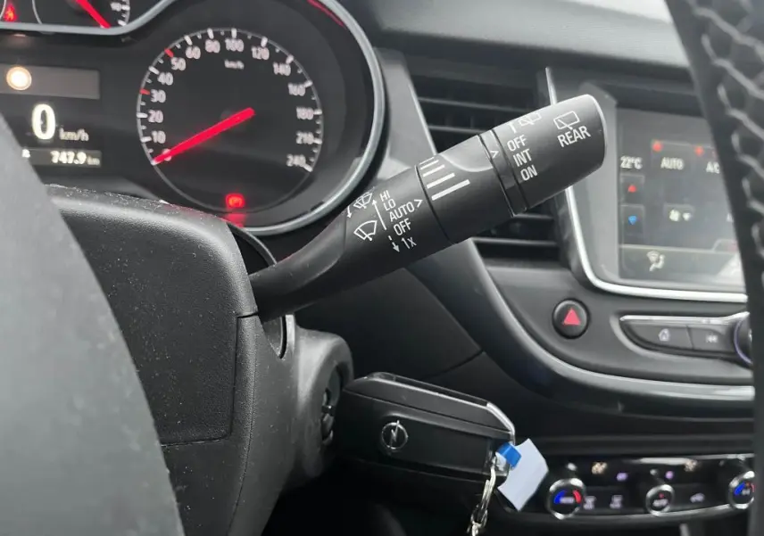 Gros plan sur le commodo d'essuie-glace à gauche du volant dans l'habitacle noir de l'Opel Crossland bleu clair 2021.