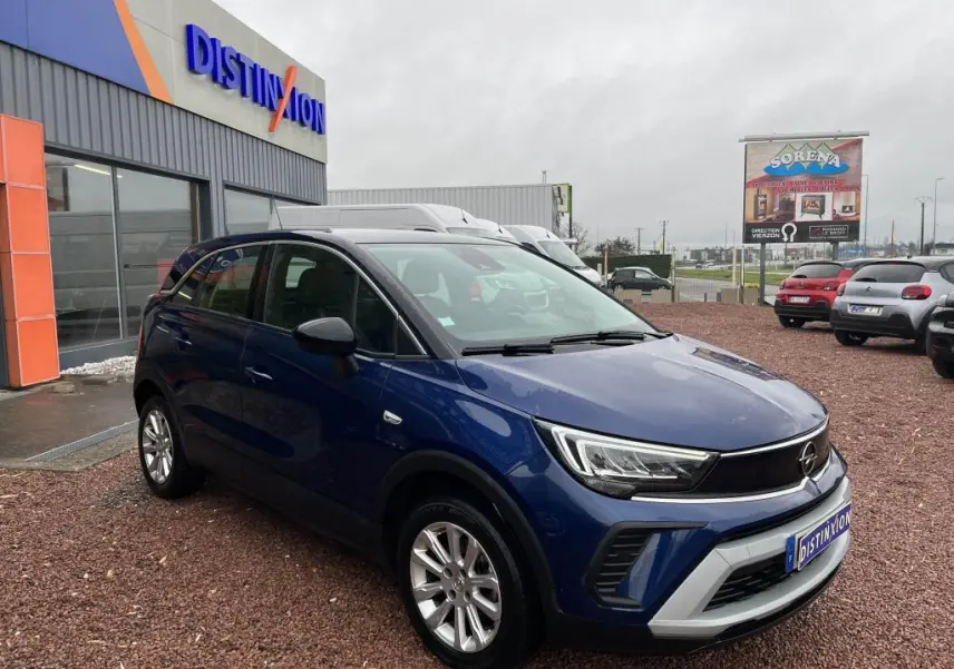 Opel Crossland bleu clair vue 3/4 avant droit avec toit noir garée devant un bâtiment commercial