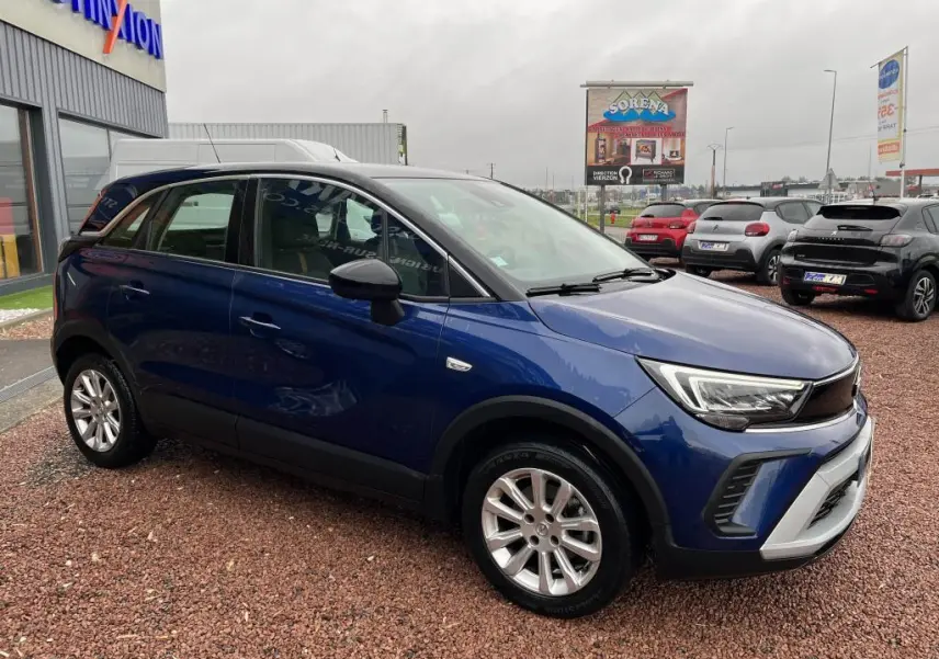 Vue 3/4 avant droite d'un Opel Crossland bleu clair avec toit noir et jantes argentées sur un parking extérieur.