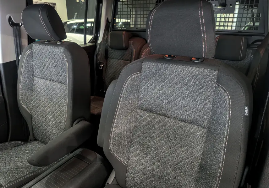 Gros plan sur les sièges avant en tissu gris et noir du Peugeot Rifter 2025, avec surpiqûres contrastantes et appuie-bras.