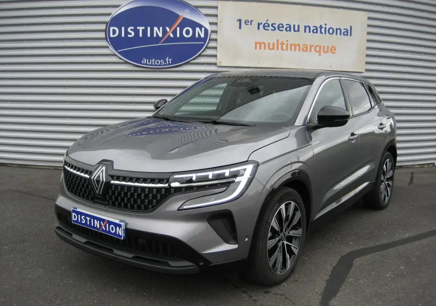 Renault Austral gris 3/4 avant droit, phares LED allumés, calandre noire et jantes bi-ton 19 pouces visibles.