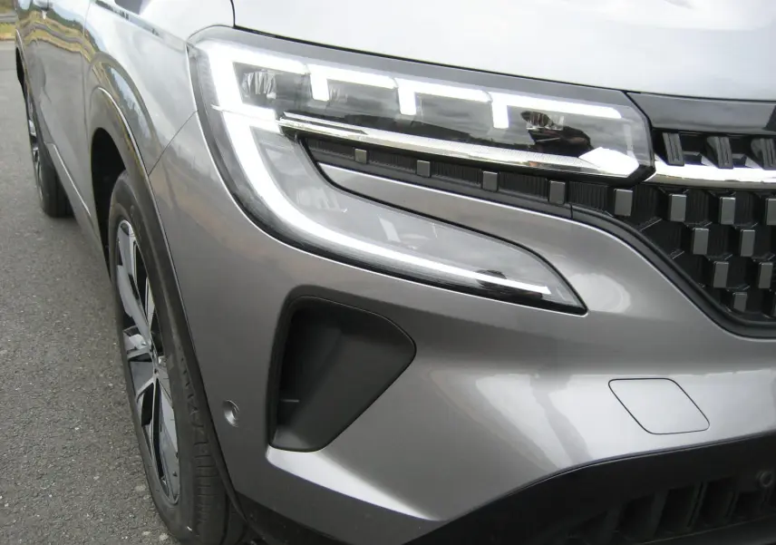 Gros plan sur l'avant gauche du Renault Austral gris 2025, mettant en valeur le phare LED et la calandre moderne.