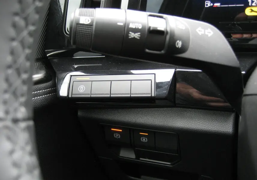 Gros plan sur la commande des feux et les boutons de sécurité du tableau de bord d’un Renault Austral gris 2025.