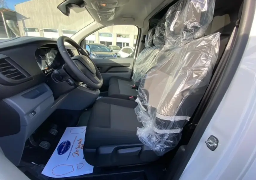 Vue intérieure côté conducteur du Peugeot Expert Fourgon blanc banquise 2023, sièges avant protégés par film plastique.