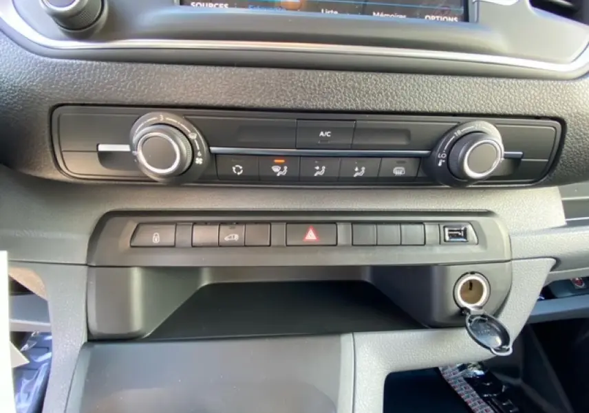 Gros plan sur la console centrale du Peugeot Expert Fourgon blanc, montrant les commandes de climatisation et les boutons de sécurité.