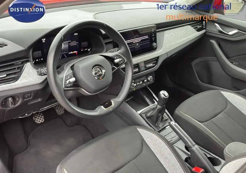 Intérieur du Skoda Kamiq 2024 montrant le poste de conduite avec volant, tableau de bord numérique et levier de vitesses manuel.