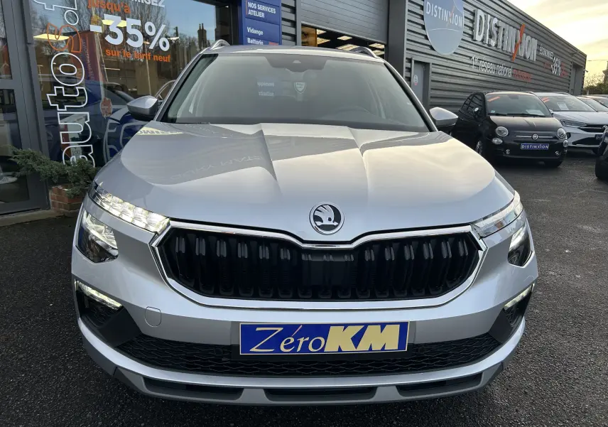 Vue avant d’un Skoda Kamiq gris argent métal 2025 avec calandre noire et phares LED allumés, en concession.