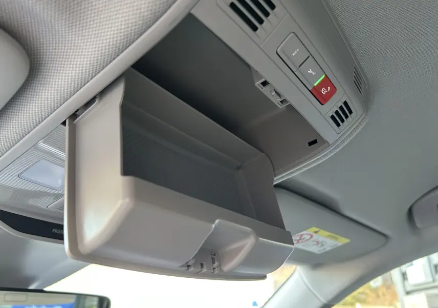 Vue intérieure en plongée du rangement lunettes ouvert gris clair au plafond d'un Skoda Kamiq 2025, avec commandes d'urgence visibles.