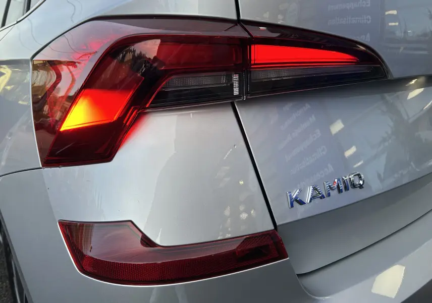 Gros plan sur le feu arrière gauche et le logo KAMIQ d'une SKODA gris argent métal, vue arrière côté gauche.