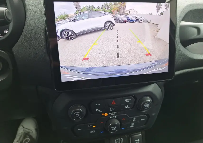 Vue intérieure centrée sur l'écran tactile montrant la caméra de recul d'une Jeep Renegade bleu 2024.