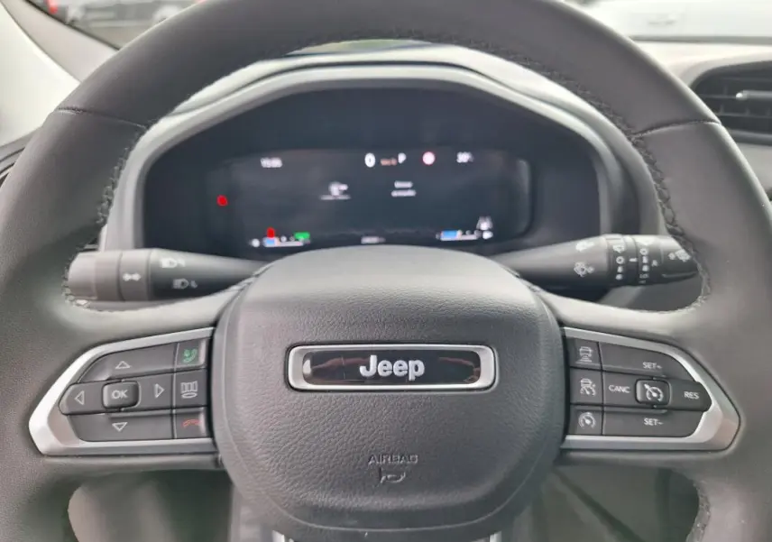 Vue rapprochée du volant noir de la Jeep Renegade 2024 avec commandes intégrées et écran numérique flou en arrière-plan.
