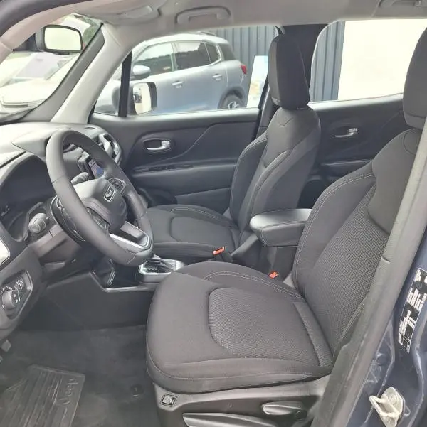 Vue intérieure côté conducteur du Jeep Renegade bleu 2024, montrant sièges noirs, volant et accoudoir central.