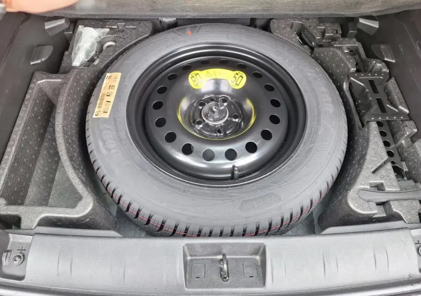 Vue plongeante sur la roue de secours noire et ses outils de bord dans le coffre du Jeep Renegade 2024.