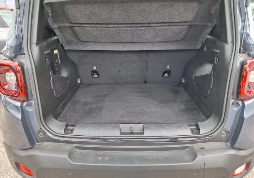 Coffre ouvert vu de l'arrière d'un Jeep Renegade bleu 2024, montrant l'espace de chargement vide et la moquette noire.