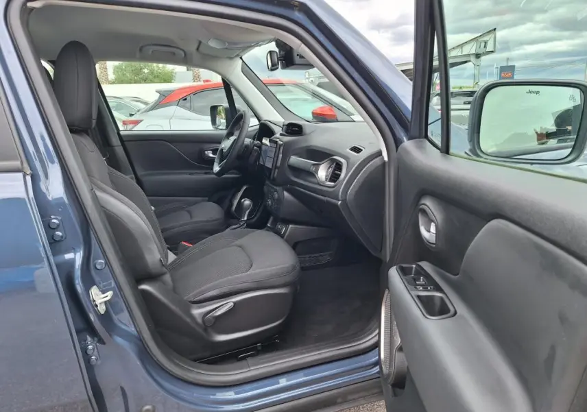 Vue intérieure côté conducteur d'un Jeep Renegade bleu 2024, montrant sièges noirs et tableau de bord moderne.
