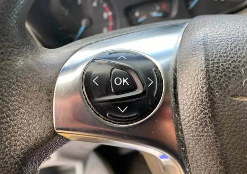 Gros plan sur les commandes au volant du Ford Transit Fourgon L3H2 2015, finition Ambiente, intérieur noir.