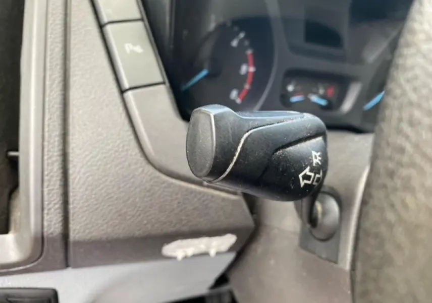 Gros plan sur la commande de clignotant noire du Ford Transit Fourgon L3H2 2015, tableau de bord gris visible en arrière-plan.