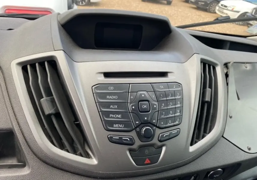 Tableau de bord central du Ford Transit Fourgon L3H2 2015 avec commandes audio et ventilation visibles, intérieur gris.