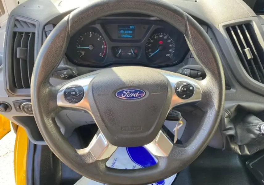Vue rapprochée du volant Ford du Transit Fourgon orange 2015, avec commandes intégrées et tableau de bord visible.