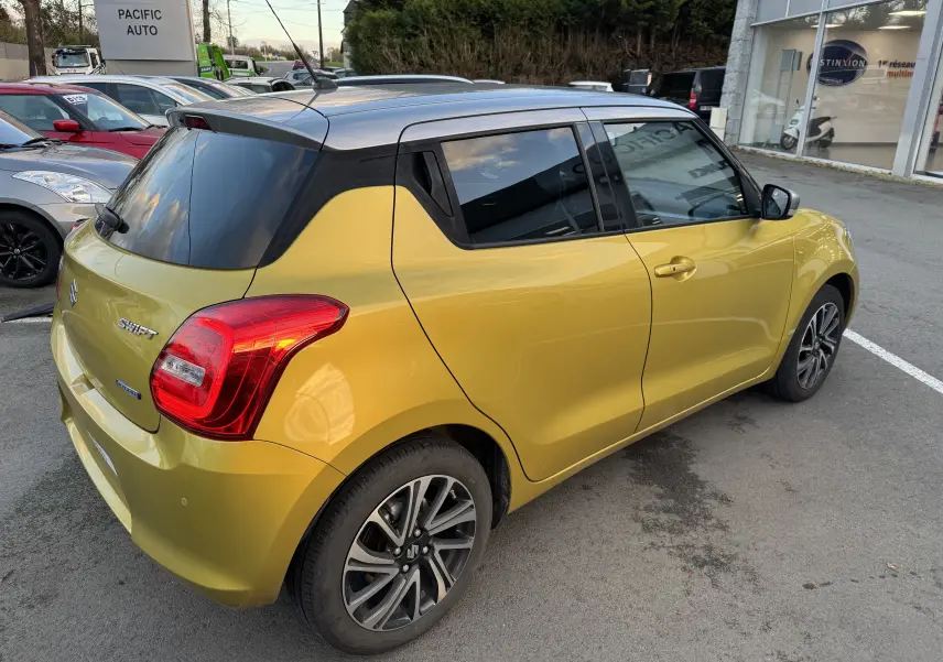 Suzuki Swift 1.2 Pack Auto 2023 jaune avec toit gris, vue 3/4 arrière côté droit sur parking extérieur.