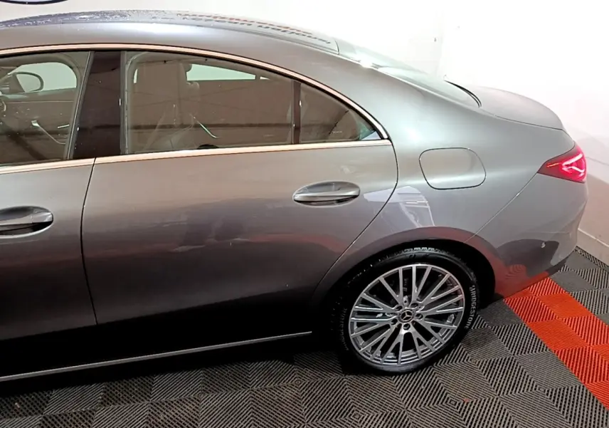 Vue côté droit arrière d'une Mercedes CLA 180 d Business Line gris clair avec jante alliage et feux arrière LED allumés.