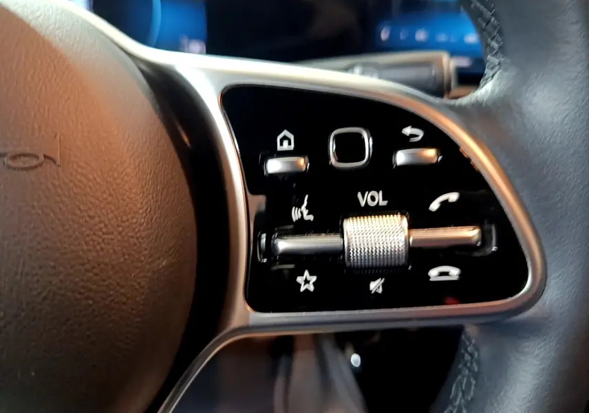 Gros plan sur les commandes multifonctions en aluminium et cuir du volant côté gauche d'une Mercedes CLA 180 d gris clair.