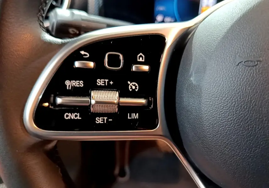 Gros plan sur les commandes de régulateur de vitesse à gauche du volant cuir noir d’une Mercedes CLA 180 d Business Line 2021.
