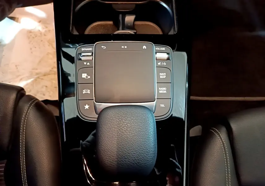 Vue plongeante sur la console centrale noire brillante avec pavé tactile et levier de vitesse cuir dans une Mercedes CLA 180 d gris clair.