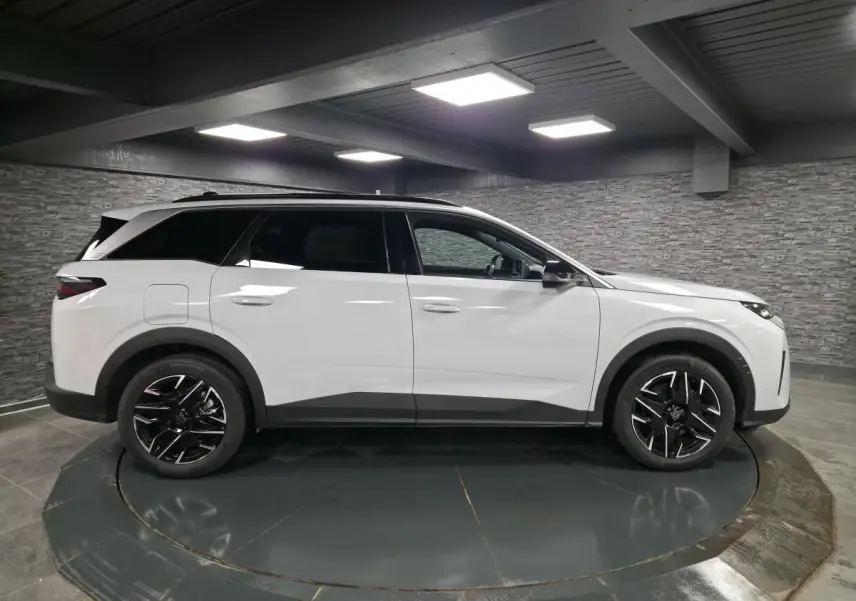 Vue latérale droite du Peugeot 5008 blanc 2025 avec jantes alliage noires et toit noir en intérieur showroom.