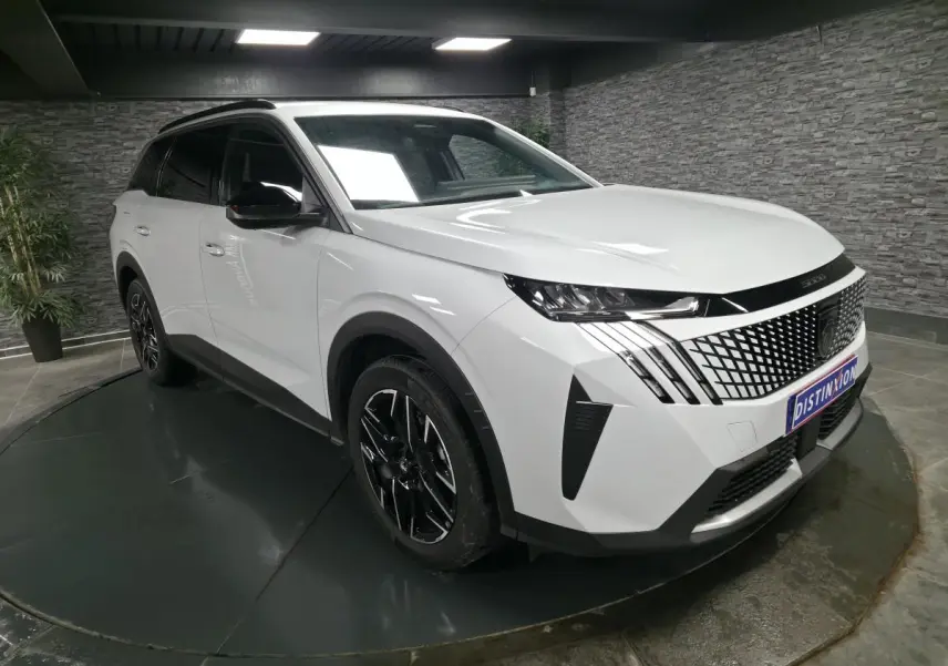 Peugeot 5008 blanc vue 3/4 avant droit avec calandre noire à motif géométrique et jantes alliage noires.